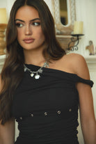 Women wearing TIC TOC AZALEA One Shoulder Mini Dress in black with twisted strap, ruching, studded detail, and flirty hemline in doors near a fire place