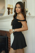 Women wearing TIC TOC AZALEA One Shoulder Mini Dress in black with twisted strap, ruching, studded detail, and flirty hemline in doors near a fire place