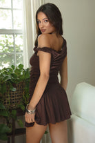 Women wearing TIC TOC AZALEA One Shoulder Mini Dress in brown with twisted strap, ruching, studded detail, and flirty hemline in doors. 