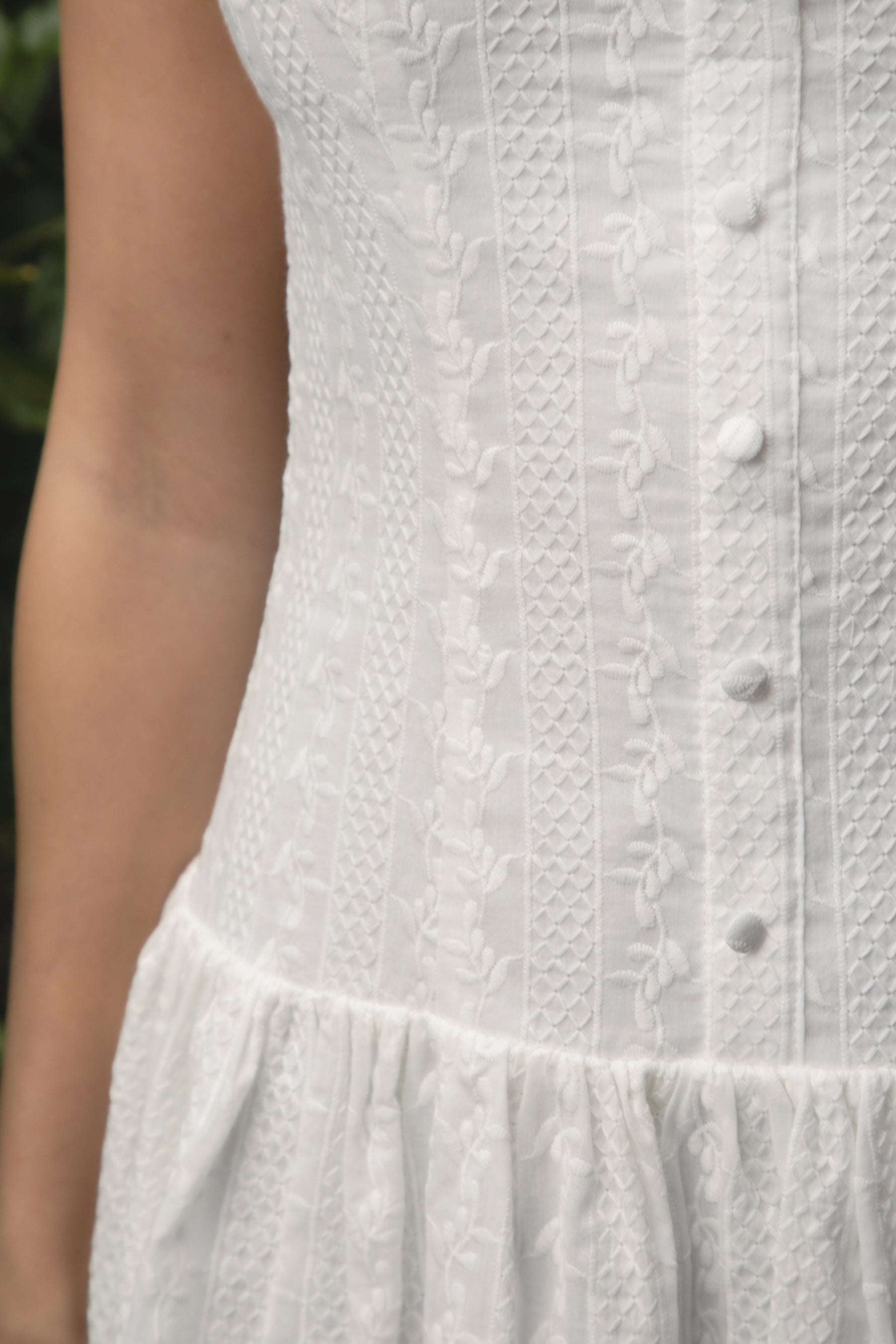 Woman wearing TIC TOC DH31913-AMABEL AMABEL embroidered drop waist mini dress made from allover eyelet embroidered cotton, featuring a clean boat neckline, sleeveless slim fit bodice, faux button front detail, drop waist seam with a flowy mini skirt, open back with zipper closure, and a lightweight fully lined construction, styled for a spring brunch or garden party look.