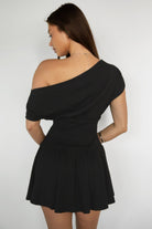 Woman wearing TIC TOC DH31921-ASHA ASHA asymmetry shirt sleeve mini dress featuring an asymmetrical one-shoulder shirt sleeve, soft cotton jersey fabrication, slouchy off-the-shoulder neckline, smocked fitted bodice, and a gathered swingy flared mini skirt, styled simply with sandals for an easy summer daytime look.