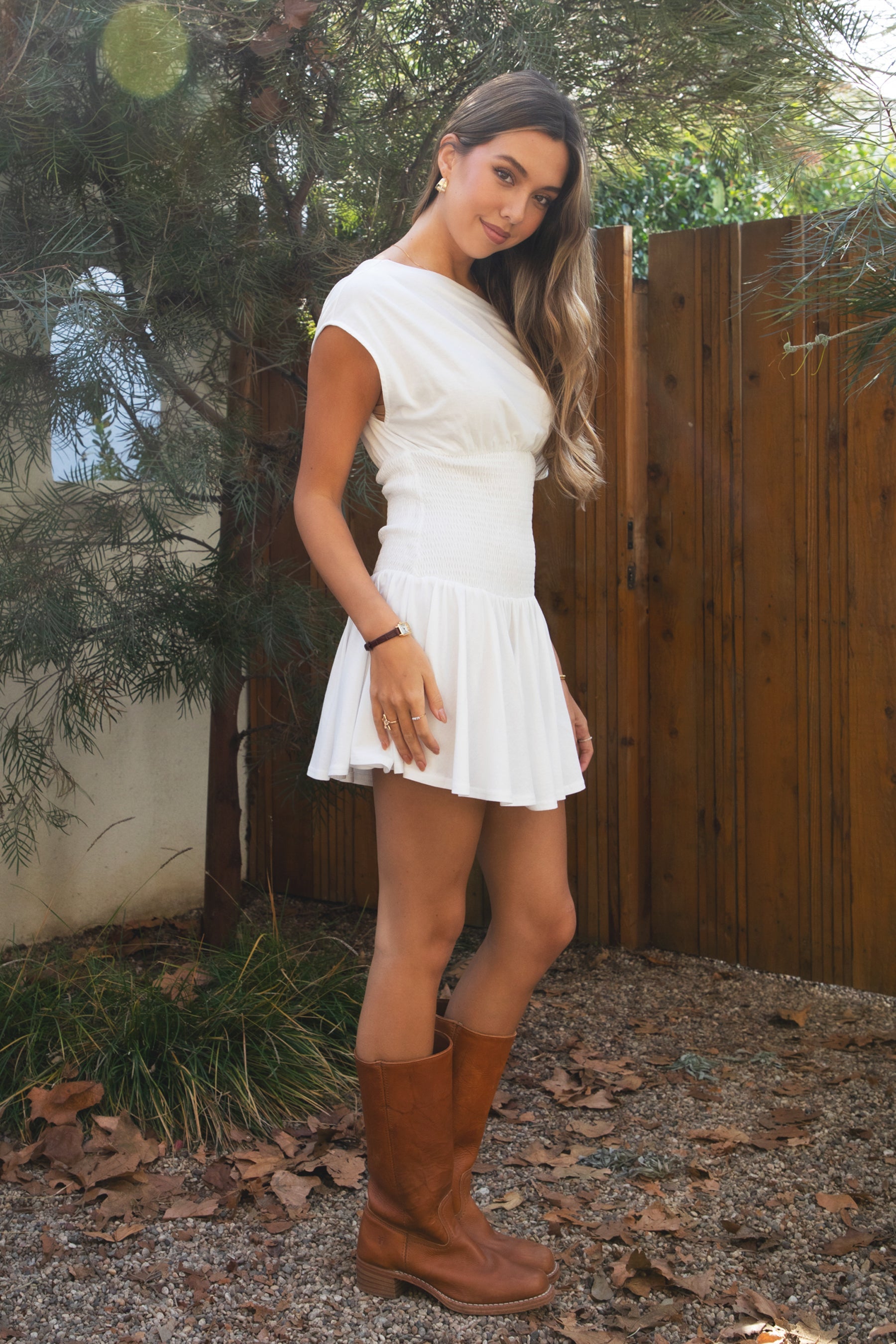 Woman wearing TIC TOC DH31921-ASHA ASHA asymmetry shirt sleeve mini dress featuring an asymmetrical one-shoulder shirt sleeve, soft cotton jersey fabrication, slouchy off-the-shoulder neckline, smocked fitted bodice, and a gathered swingy flared mini skirt, styled simply with sandals for an easy summer daytime look.