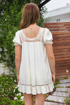 Woman wearing EVANGELIN sheer satin short sleeve mini dress featuring a romantic scoop neckline with sheer lace trim, soft satin babydoll silhouette, puff sleeves with elastic lace cuffs, front self tie bow, lace contrast panels, and ruffle hem finish for bridal and romantic occasion styling.