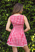 Woman wearing CHERYN V-neck gingham poplin mini dress featuring a classic gingham check pattern, scalloped lace trim neckline, sleeveless fit-and-flare bodice, decorative faux button detail, smocked back panel, hidden side zipper, and floral eyelet lace hem.