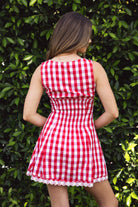 Woman wearing CHERYN V-neck gingham poplin mini dress featuring a classic gingham check pattern, scalloped lace trim neckline, sleeveless fit-and-flare bodice, decorative faux button detail, smocked back panel, hidden side zipper, and floral eyelet lace hem.