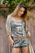 Woman wearing GLITZWOOD camo print sequin jersey halter tank featuring stretch jersey fabric, woodland camo print, subtle micro sequin finish, self tie halter neckline, open back detail, and a body skimming silhouette with soft milk lining for festival-ready styling.