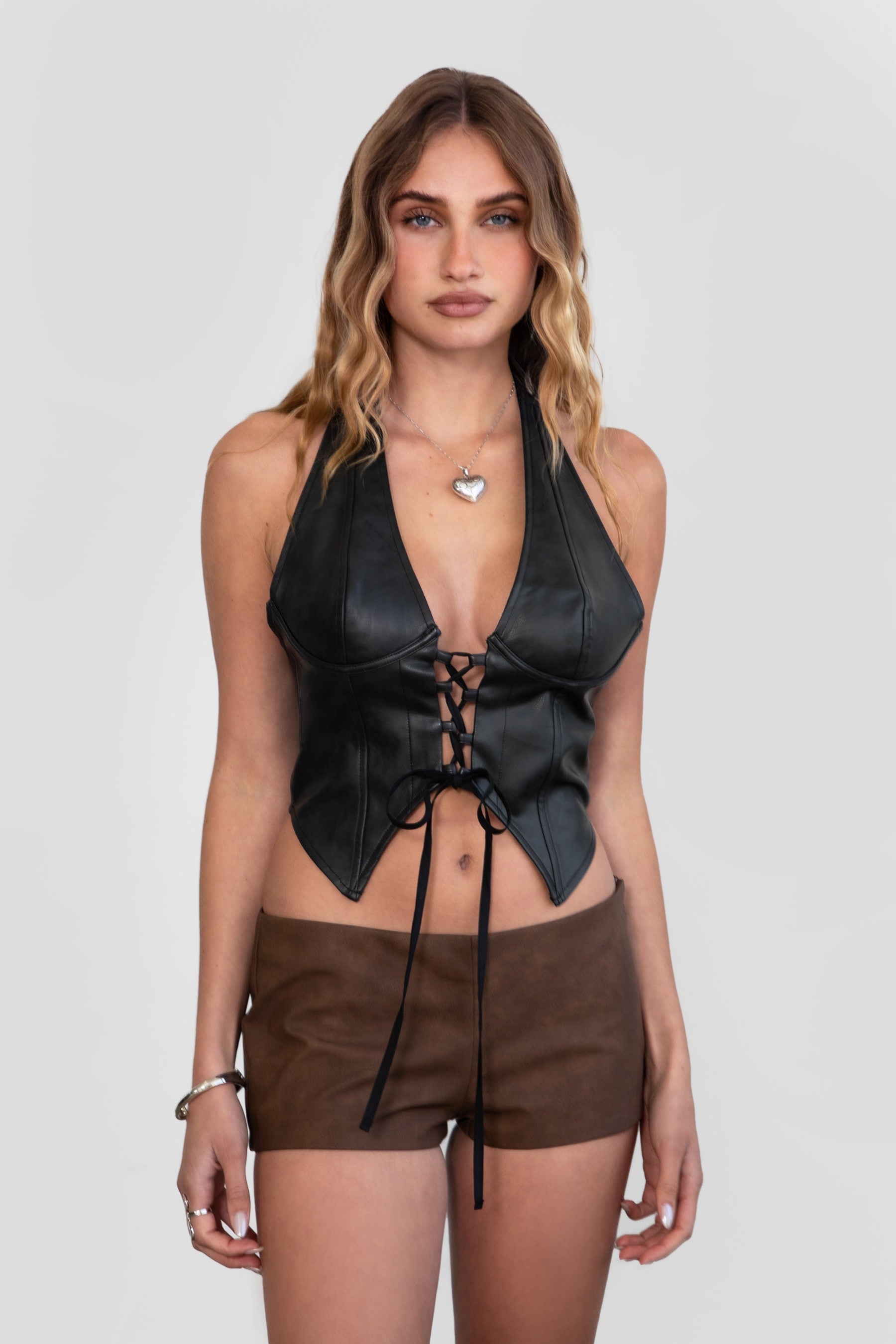 Model wearing LEIAH vegan leather micro shorts in black and brown, styled for a Western festival look