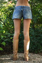 Woman wearing TIC TOC PF31908 LIVANE low rise micro denim mini shorts featuring washed denim fabric with a soft vintage feel, a low rise waist, clean hem finish, classic five pocket styling, and a flirty micro mini length for an easy Y2K-inspired summer look.