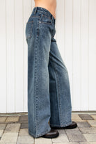 Woman wearing STERLING rhinestone straight leg jean featuring premium cotton denim, allover sparkling rhinestone embellishments, mid rise waist, relaxed straight leg silhouette, subtle vintage wash, classic five pocket design, zip fly, and button closure for statement styling.