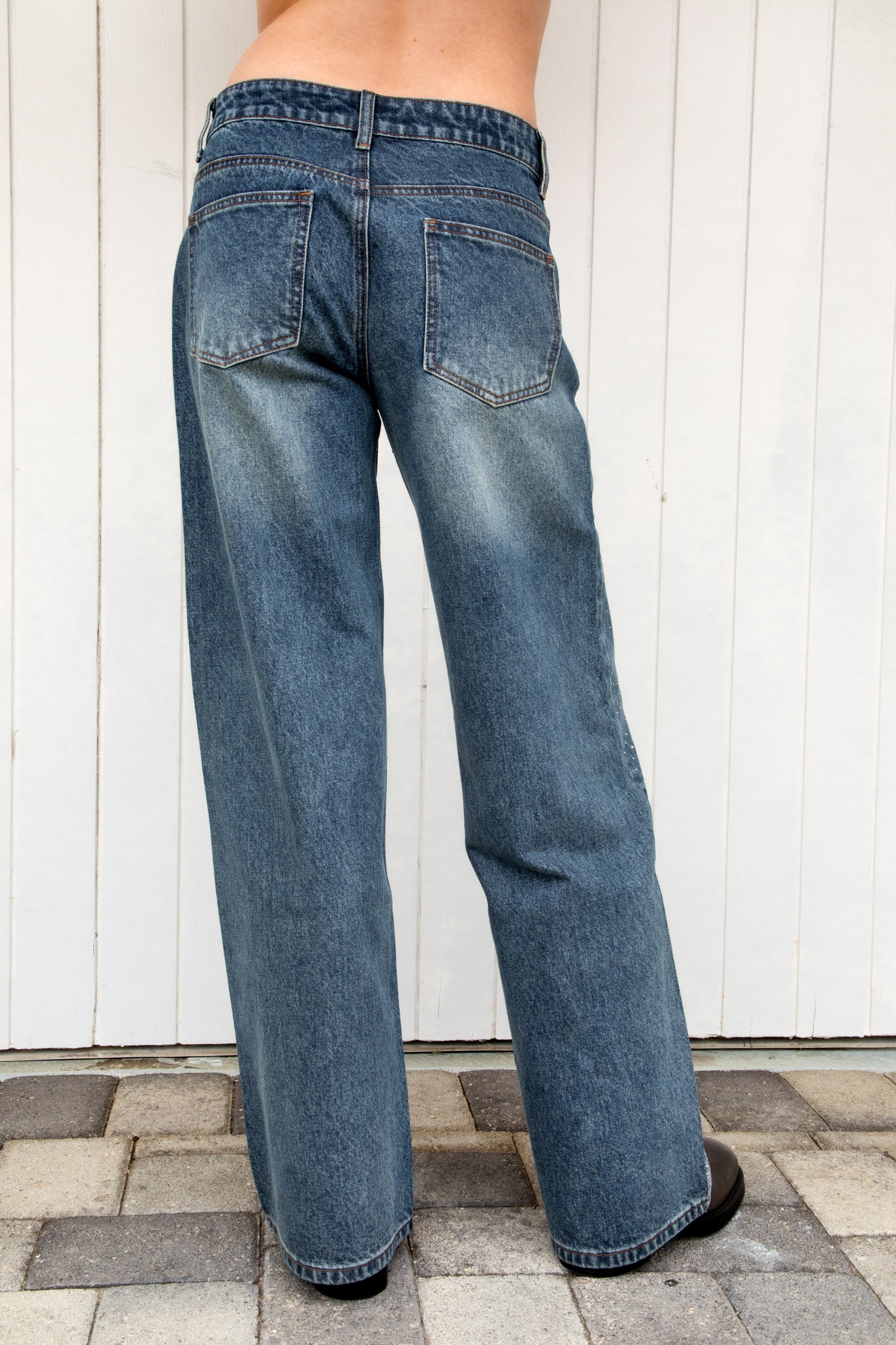 Woman wearing STERLING rhinestone straight leg jean featuring premium cotton denim, allover sparkling rhinestone embellishments, mid rise waist, relaxed straight leg silhouette, subtle vintage wash, classic five pocket design, zip fly, and button closure for statement styling.