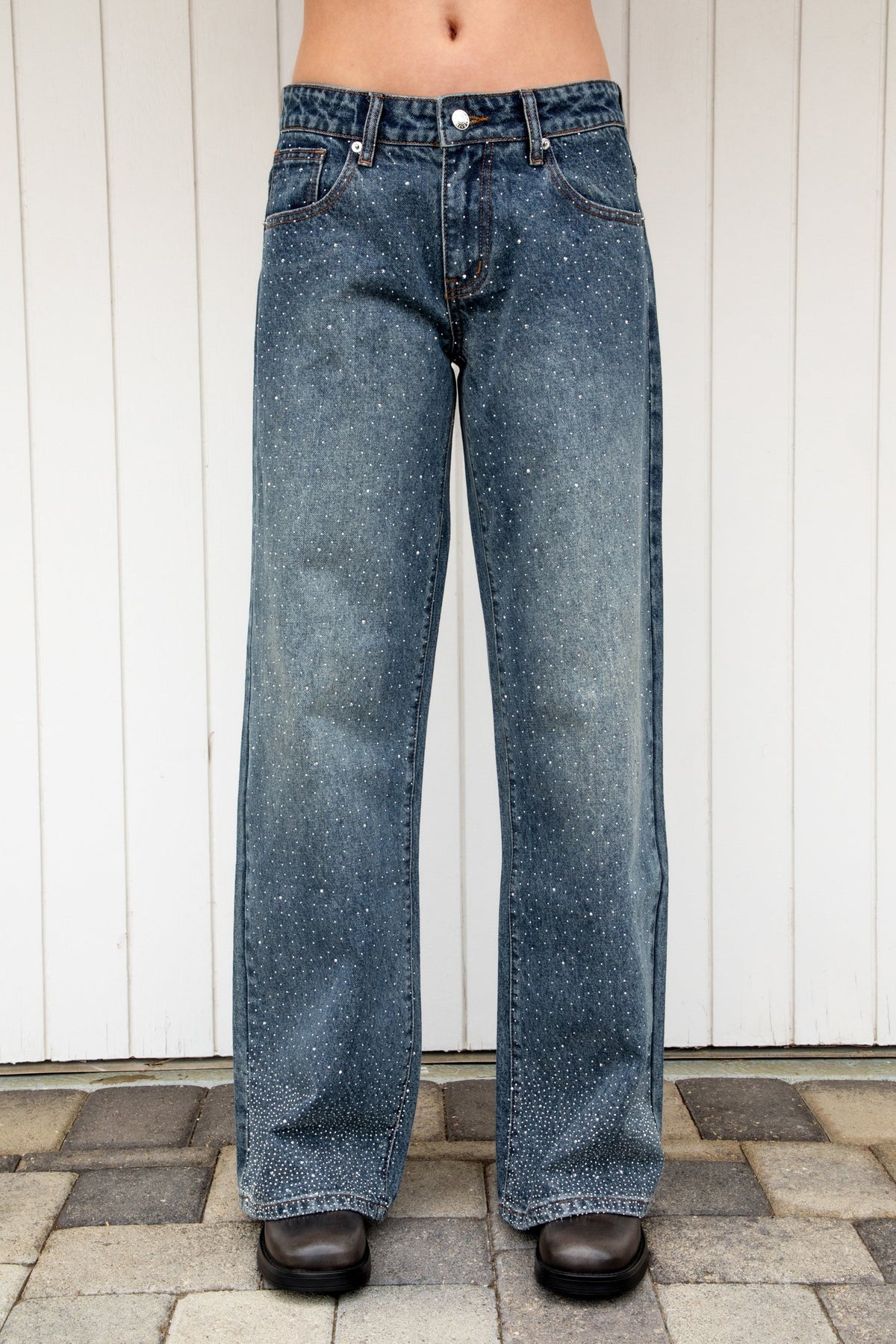 Woman wearing STERLING rhinestone straight leg jean featuring premium cotton denim, allover sparkling rhinestone embellishments, mid rise waist, relaxed straight leg silhouette, subtle vintage wash, classic five pocket design, zip fly, and button closure for statement styling.
