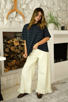 Woman wearing POSIE ruffle hem wide leg pants featuring soft cotton denim, relaxed mid rise fit, classic five pocket design, button and zip closure, and a feminine ruffle hem detail for easy casual styling with tanks, blouses, and cropped knit tops.