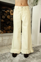 Woman wearing POSIE ruffle hem wide leg pants featuring soft cotton denim, relaxed mid rise fit, classic five pocket design, button and zip closure, and a feminine ruffle hem detail for easy casual styling with tanks, blouses, and cropped knit tops.