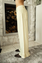 Woman wearing POSIE ruffle hem wide leg pants featuring soft cotton denim, relaxed mid rise fit, classic five pocket design, button and zip closure, and a feminine ruffle hem detail for easy casual styling with tanks, blouses, and cropped knit tops.