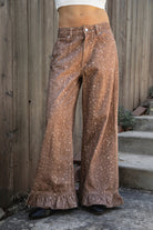 Woman wearing DOE deer printed ruffle hem wide leg denim pants featuring structured cotton print denim, high rise waist, button and zip fly closure, allover fawn inspired speckled print, wide leg silhouette, ruffle hem detail, classic five pocket design, and belt loops for western statement styling.