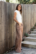 Woman wearing DOE deer printed ruffle hem wide leg denim pants featuring structured cotton print denim, high rise waist, button and zip fly closure, allover fawn inspired speckled print, wide leg silhouette, ruffle hem detail, classic five pocket design, and belt loops for western statement styling.
