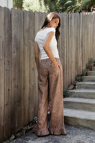 Woman wearing DOE deer printed ruffle hem wide leg denim pants featuring structured cotton print denim, high rise waist, button and zip fly closure, allover fawn inspired speckled print, wide leg silhouette, ruffle hem detail, classic five pocket design, and belt loops for western statement styling.