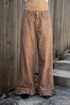 Woman wearing DOE deer printed ruffle hem wide leg denim pants featuring structured cotton print denim, high rise waist, button and zip fly closure, allover fawn inspired speckled print, wide leg silhouette, ruffle hem detail, classic five pocket design, and belt loops for western statement styling.