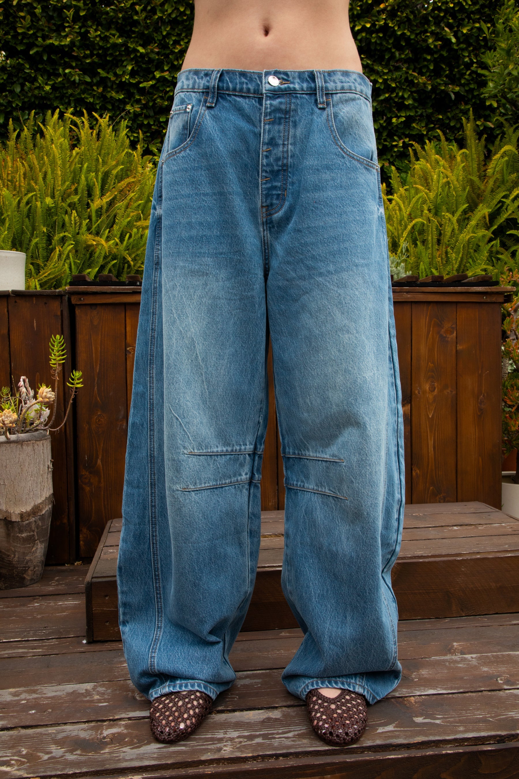 Woman wearing ROMII mid rise baggy fit barrel jeans featuring soft cotton lyocell denim, relaxed barrel leg silhouette, panel seam detailing, subtle knee tucks, classic five pocket design, zip fly, and button closure for modern casual streetwear styling.