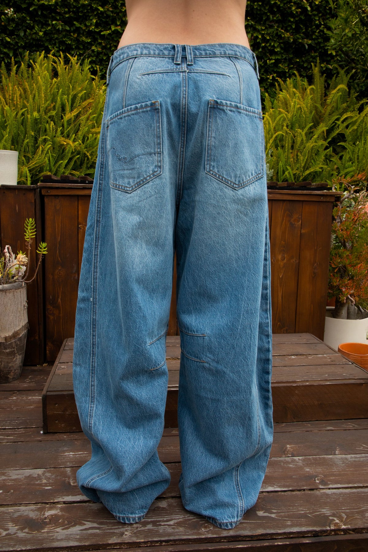 Woman wearing ROMII mid rise baggy fit barrel jeans featuring soft cotton lyocell denim, relaxed barrel leg silhouette, panel seam detailing, subtle knee tucks, classic five pocket design, zip fly, and button closure for modern casual streetwear styling.