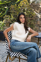 Woman wearing GARANCE mock neck sleeveless sweater top featuring a soft fuzzy knit texture, clean minimalist silhouette, polished mock neckline, relaxed bodice, subtle extended shoulder design, cropped length, wide ribbed hem, and solid color design for easy transitional layering.