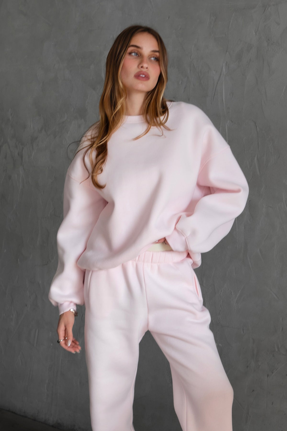 Person wearing a pale pink sweater and pants set on a white background