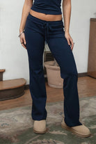 Woman wearing TIC TOC PH31905BA-NYLEE-WL navy NYLEE WL wide leg pants made from soft span jersey fabric, featuring a high-stretch body-hugging fit through the hips, foldover waistband with tie detail, and full-length wide leg silhouette, styled indoors with a matching top for a coordinated lounge/athleisure look.