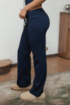 Woman wearing TIC TOC PH31905BA-NYLEE-WL navy NYLEE WL wide leg pants made from soft span jersey fabric, featuring a high-stretch body-hugging fit through the hips, foldover waistband with tie detail, and full-length wide leg silhouette, styled indoors with a matching top for a coordinated lounge/athleisure look.