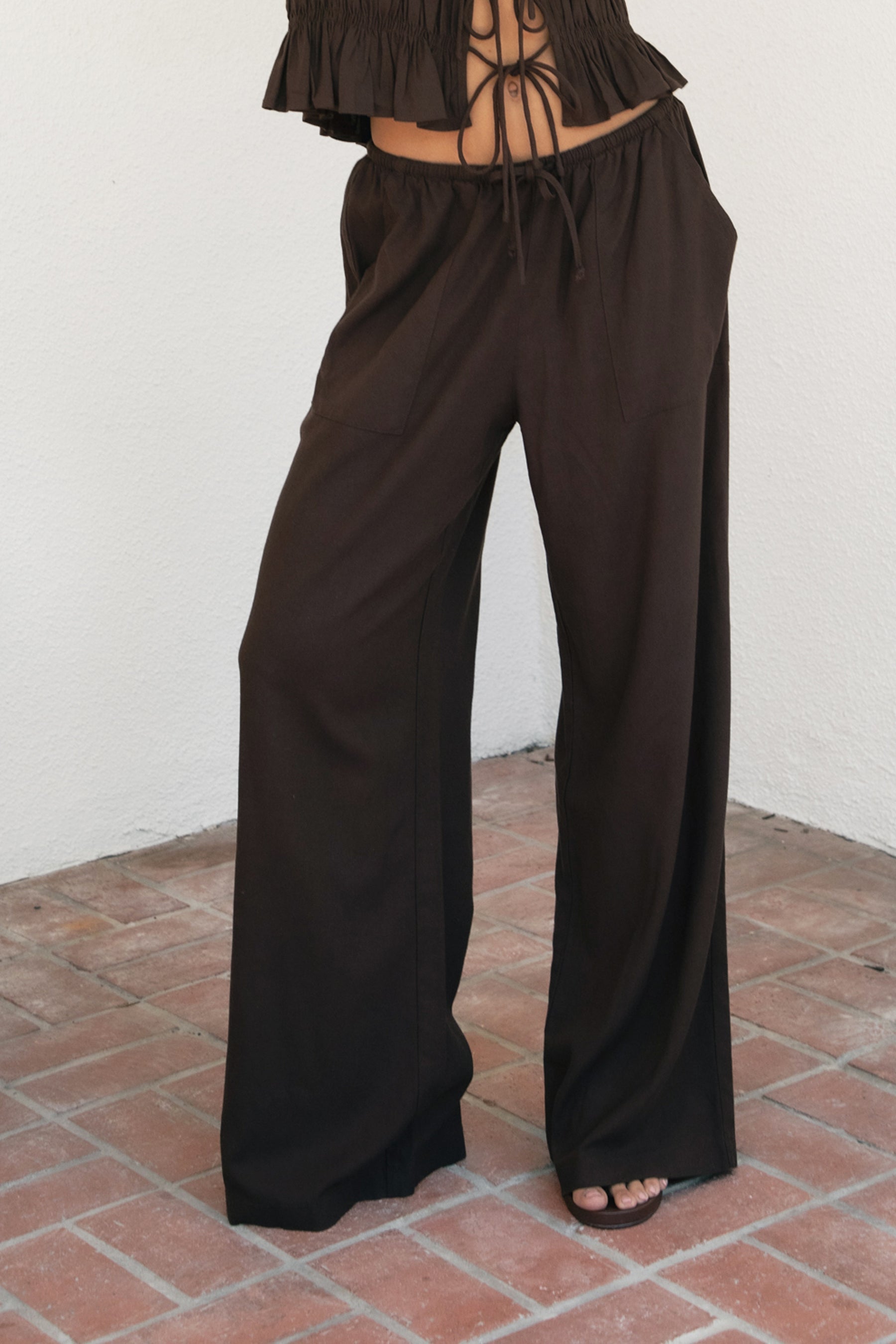 Woman wearing SOLSTICE viscose linen drawstring wide leg pants featuring a relaxed flowy silhouette, elastic waistband with adjustable drawstring, functional side pockets, back patch pockets, and lightweight breathable viscose linen fabric for effortless resort styling.