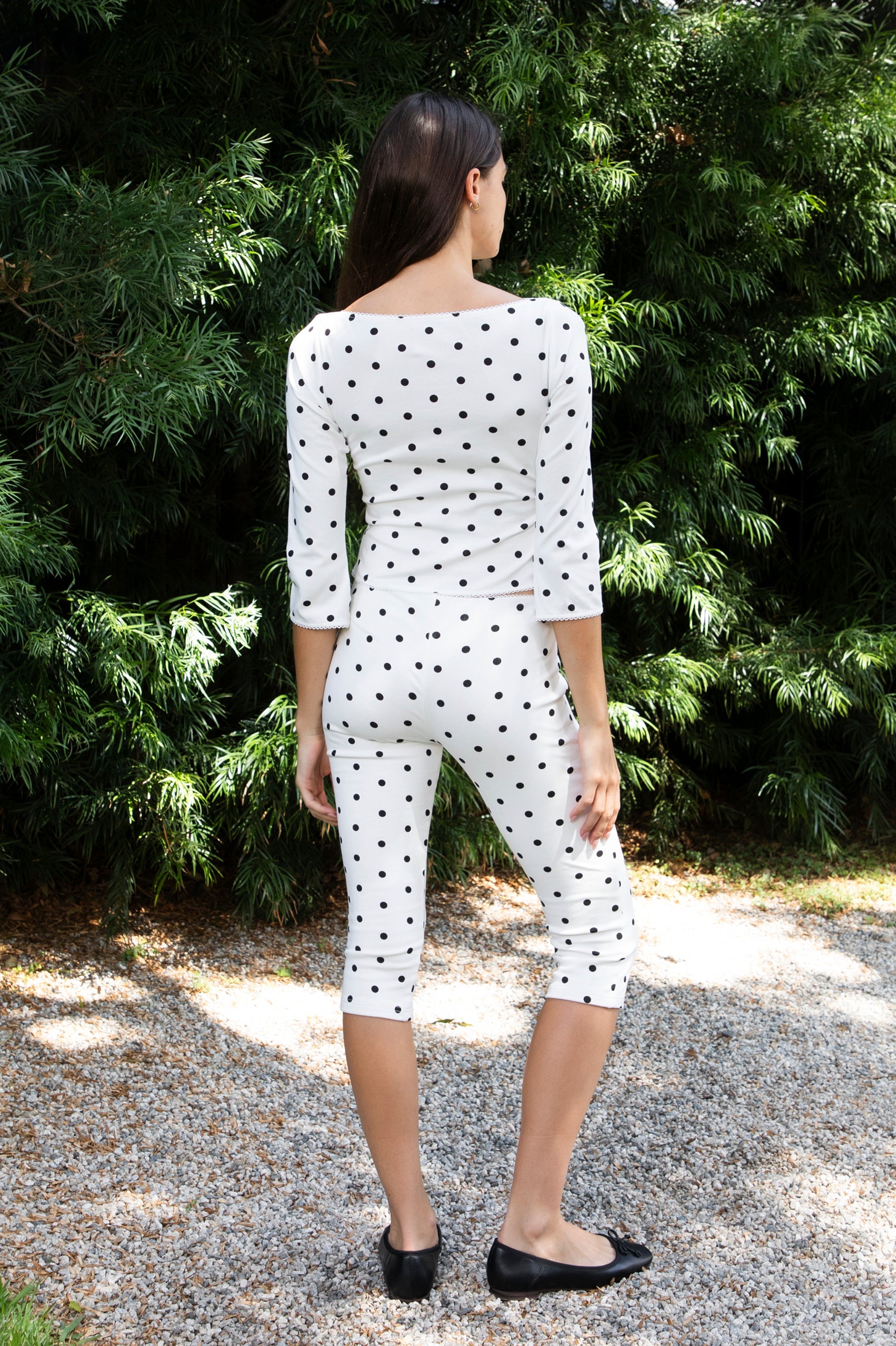 Woman wearing MARIE polka dot capri pants featuring soft cotton stretch jersey fabric, allover polka dot print, mid rise waist, clean pull on design, slim fitted silhouette through the hip and leg, cropped capri length, and delicate picot trim along the waistband designed to pair with the matching MARIE top.