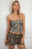 Woman wearing a camouflage outfit standing against a white wall.