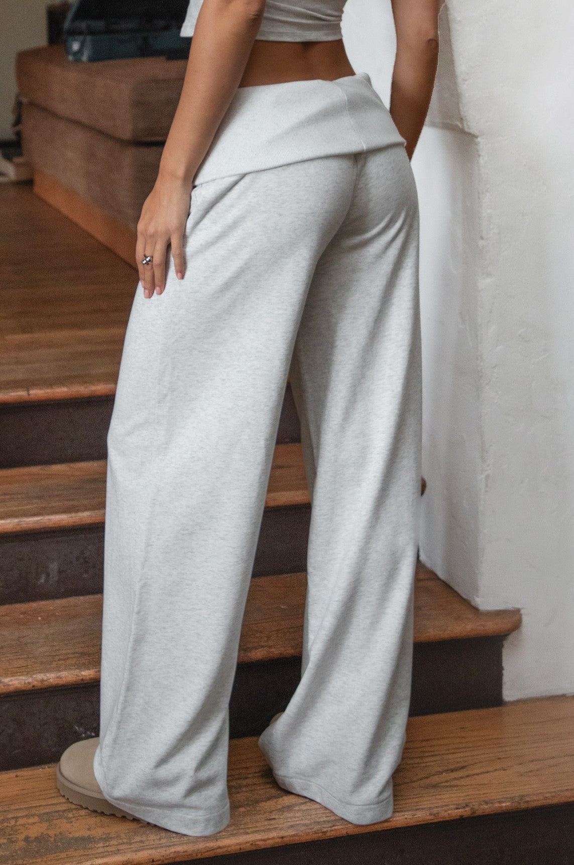 Woman wearing TIC TOC PJ31587BA COVE heather white wide leg lounge pants featuring a foldover waistband with logo detail, relaxed loose silhouette, wide leg shape, and side pockets, styled indoors with matching crop top and fur-trim hoodie.