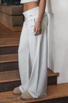 Woman wearing TIC TOC PJ31587BA COVE heather white wide leg lounge pants featuring a foldover waistband with logo detail, relaxed loose silhouette, wide leg shape, and side pockets, styled indoors with matching crop top and fur-trim hoodie.
