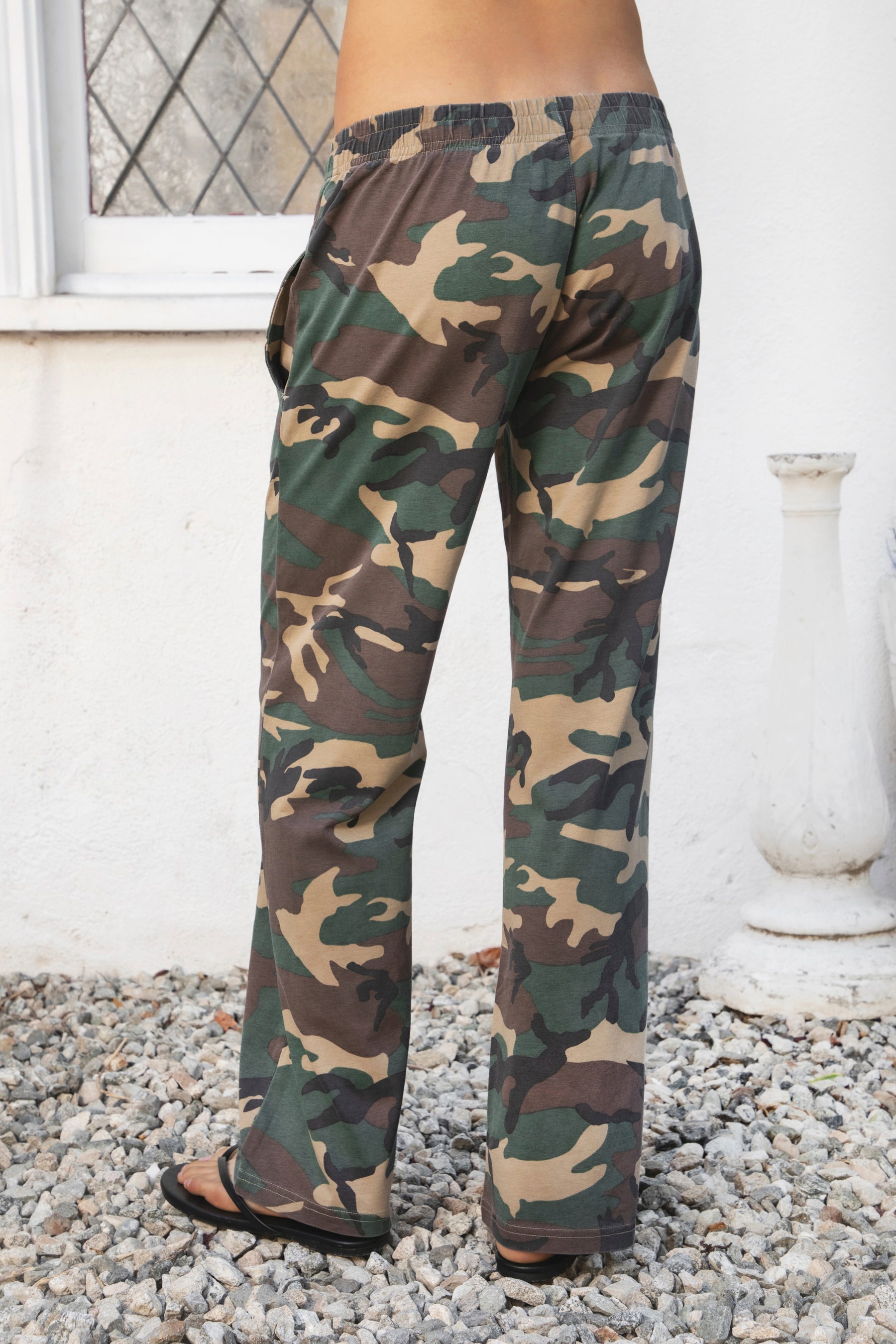 Woman wearing SCOUT military camo washed jersey wide leg pants featuring soft washed cotton jersey fabric, allover classic military camouflage print, comfortable elastic waistband, relaxed straight leg silhouette, functional side pockets, and full length design for laid back casual styling.