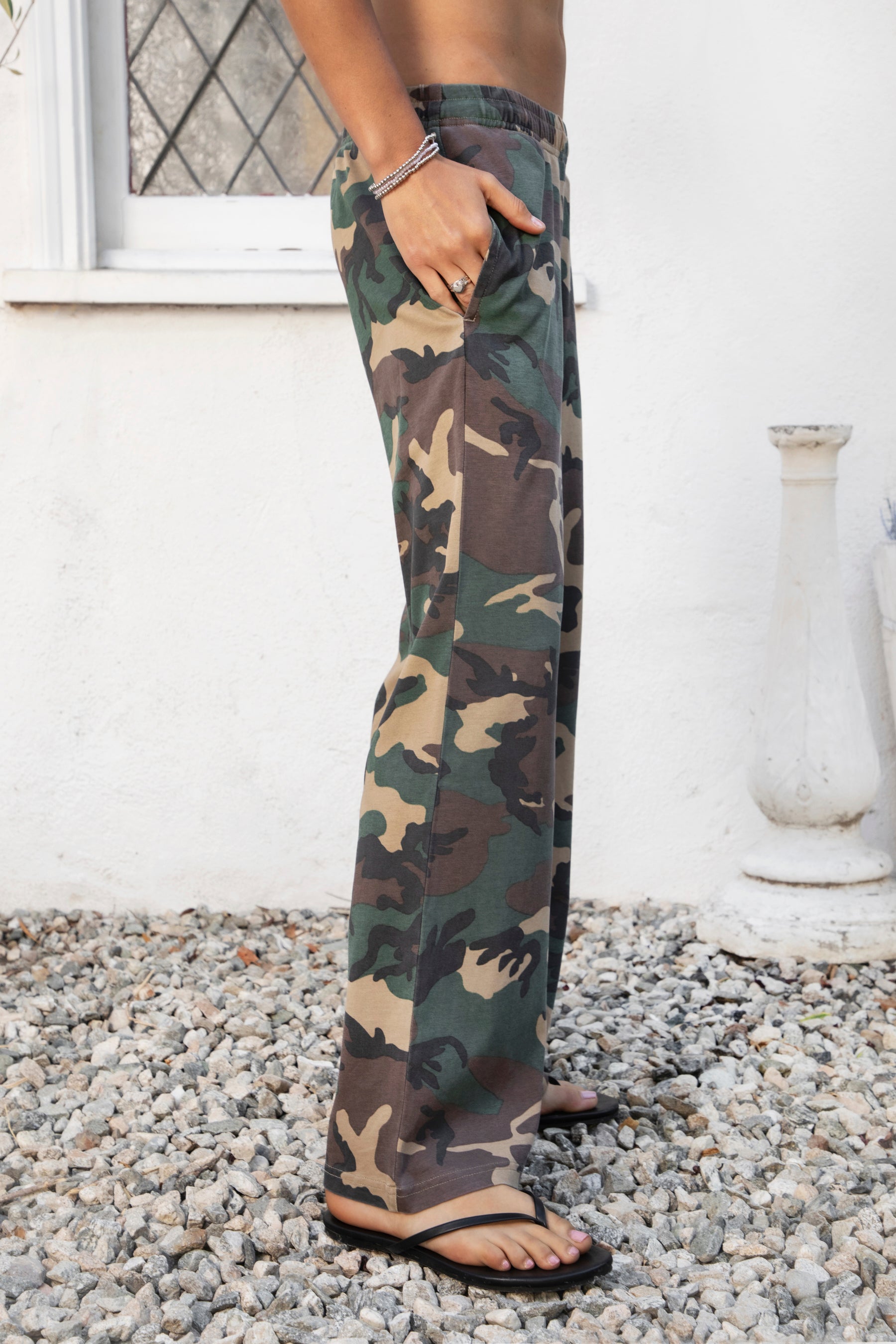 Woman wearing SCOUT military camo washed jersey wide leg pants featuring soft washed cotton jersey fabric, allover classic military camouflage print, comfortable elastic waistband, relaxed straight leg silhouette, functional side pockets, and full length design for laid back casual styling.