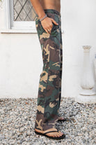 Woman wearing SCOUT military camo washed jersey wide leg pants featuring soft washed cotton jersey fabric, allover classic military camouflage print, comfortable elastic waistband, relaxed straight leg silhouette, functional side pockets, and full length design for laid back casual styling.