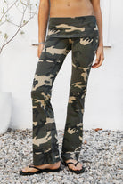 Woman wearing REMI dark military camo fold over flare leggings featuring soft stretch cotton jersey fabric, allover classic military camouflage print, low rise fit, wide fold over waistband, fitted hips and thighs, flared leg, garment washed finish, and full length pull on silhouette.