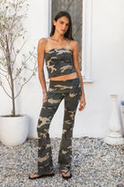 Woman wearing REMI dark military camo fold over flare leggings featuring soft stretch cotton jersey fabric, allover classic military camouflage print, low rise fit, wide fold over waistband, fitted hips and thighs, flared leg, garment washed finish, and full length pull on silhouette.