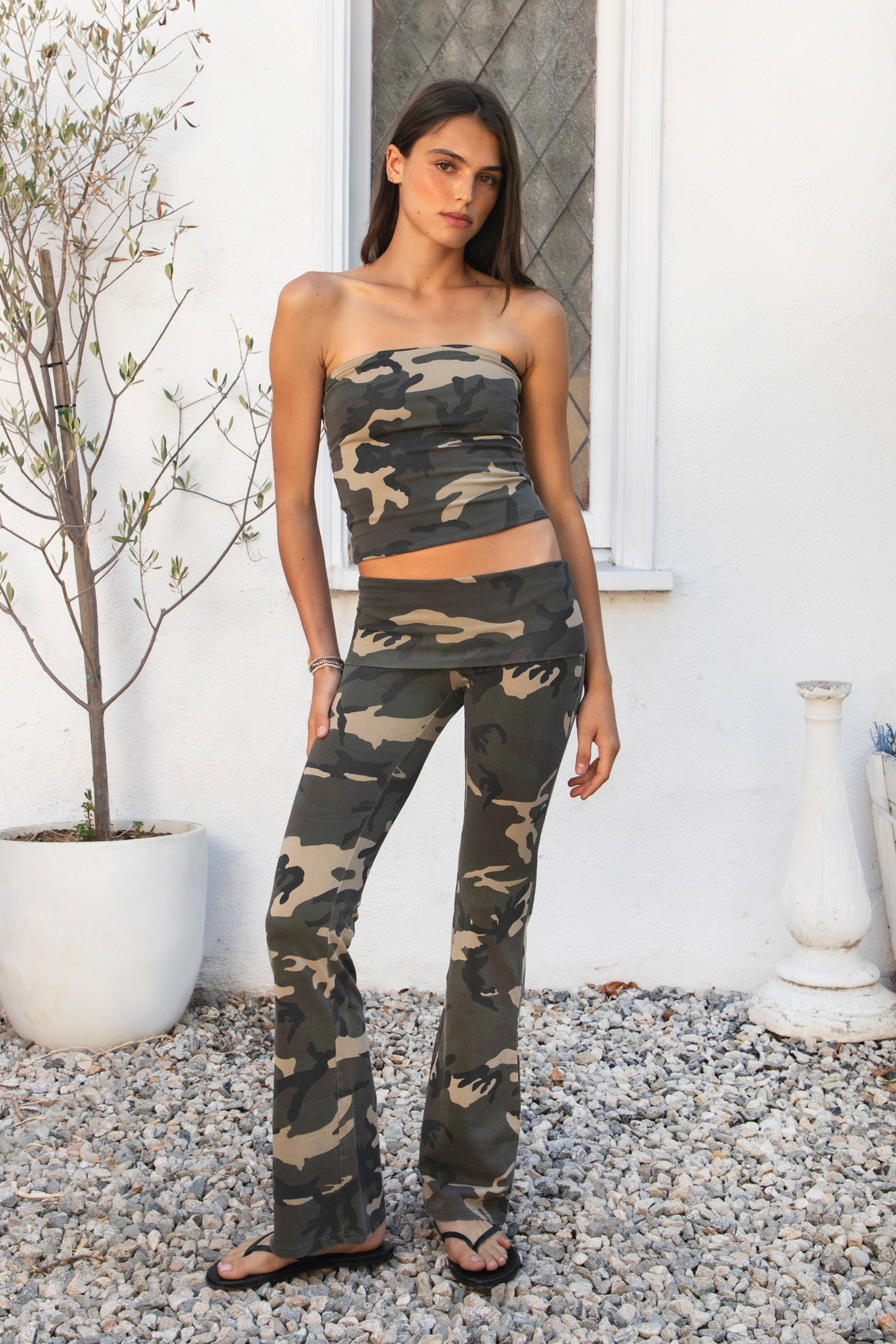 Woman wearing REMI dark military camo fold over flare leggings featuring soft stretch cotton jersey fabric, allover classic military camouflage print, low rise fit, wide fold over waistband, fitted hips and thighs, flared leg, garment washed finish, and full length pull on silhouette.