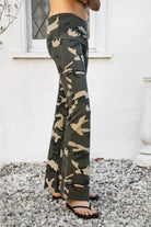 Woman wearing REMI dark military camo fold over flare leggings featuring soft stretch cotton jersey fabric, allover classic military camouflage print, low rise fit, wide fold over waistband, fitted hips and thighs, flared leg, garment washed finish, and full length pull on silhouette.