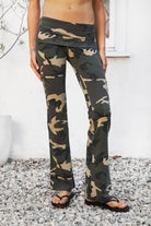 Woman wearing REMI dark military camo fold over flare leggings featuring soft stretch cotton jersey fabric, allover classic military camouflage print, low rise fit, wide fold over waistband, fitted hips and thighs, flared leg, garment washed finish, and full length pull on silhouette.