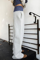 Woman wearing COSETTE polka dot waist wide leg sweatpants featuring soft fleece fabric, relaxed wide leg silhouette, contrast navy ribbed waistband with allover white polka dot pattern, high rise statement fit, soft heather grey body, full length design, functional side pockets, and matching set styling.
