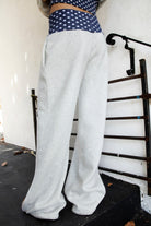 Woman wearing COSETTE polka dot waist wide leg sweatpants featuring soft fleece fabric, relaxed wide leg silhouette, contrast navy ribbed waistband with allover white polka dot pattern, high rise statement fit, soft heather grey body, full length design, functional side pockets, and matching set styling.