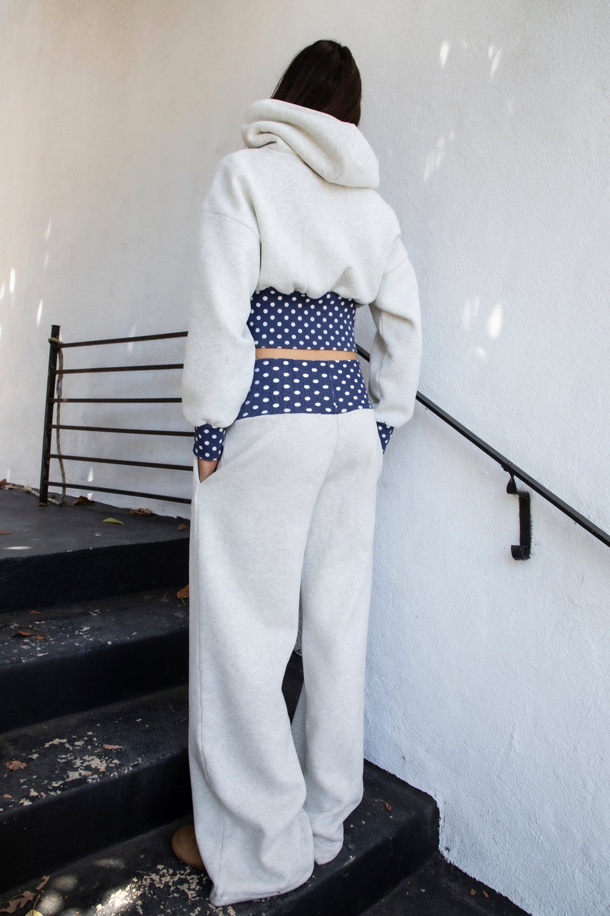 Woman wearing COSETTE polka dot waist wide leg sweatpants featuring soft fleece fabric, relaxed wide leg silhouette, contrast navy ribbed waistband with allover white polka dot pattern, high rise statement fit, soft heather grey body, full length design, functional side pockets, and matching set styling.