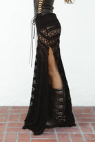 Woman wearing MARISS stretch lace side slit long skirt featuring sheer stretch lace fabric, flowy silhouette with airy movement, high side slit, picot trim waistband, and built-in micro shorts lining for coverage and comfort.