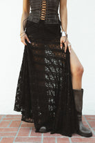 Woman wearing MARISS stretch lace side slit long skirt featuring sheer stretch lace fabric, flowy silhouette with airy movement, high side slit, picot trim waistband, and built-in micro shorts lining for coverage and comfort.
