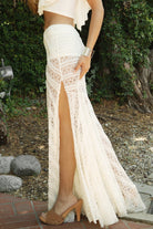 Woman wearing MARISS stretch lace side slit long skirt featuring sheer stretch lace fabric, flowy silhouette with airy movement, high side slit, picot trim waistband, and built-in micro shorts lining for coverage and comfort.