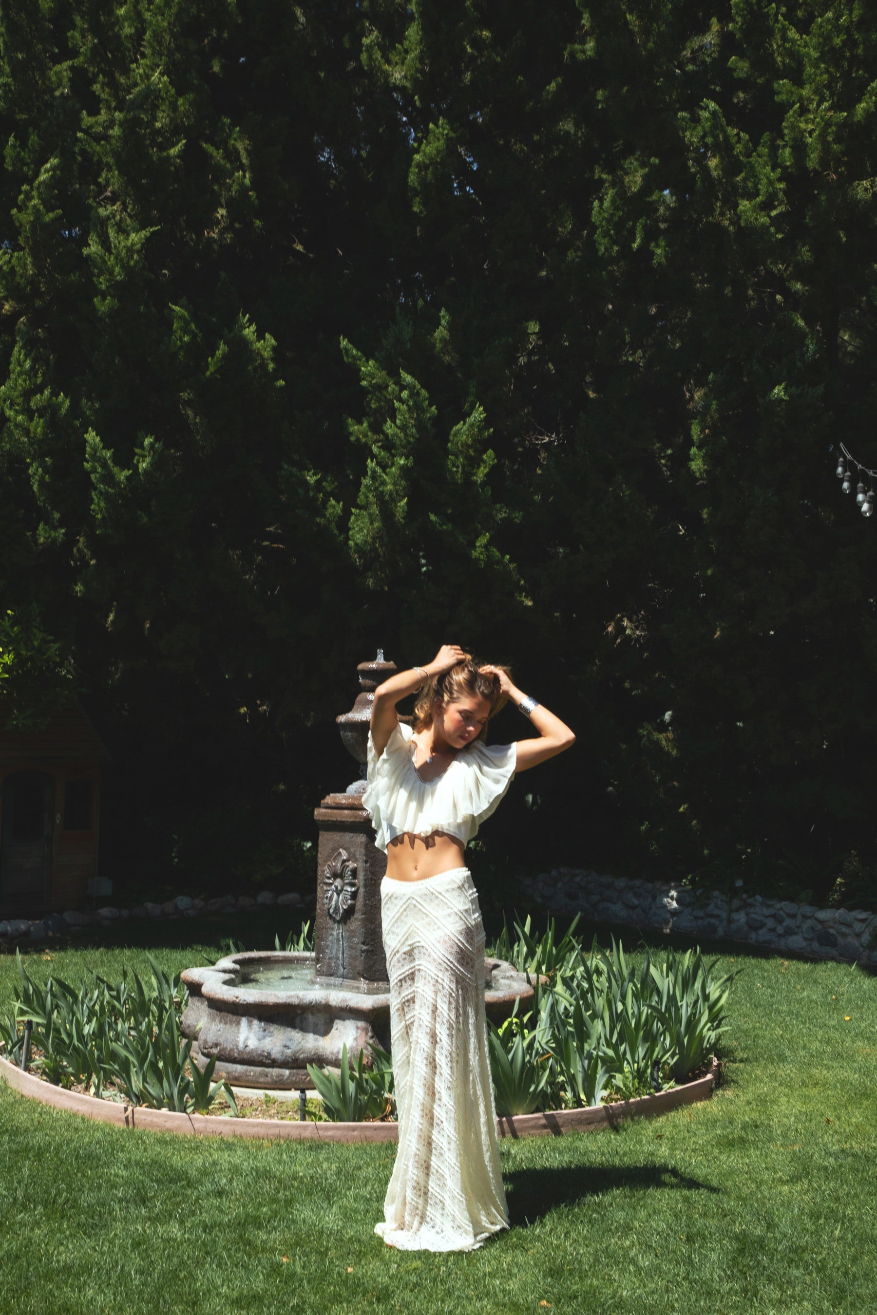 Woman wearing MARISS stretch lace side slit long skirt featuring sheer stretch lace fabric, flowy silhouette with airy movement, high side slit, picot trim waistband, and built-in micro shorts lining for coverage and comfort.