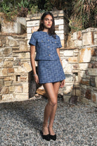 Woman wearing COCO navy blue lurex tweed skort featuring shimmering textured tweed fabric, subtle metallic lurex detail, mini length, skirt inspired front with hidden shorts comfort, clean fitted waist, side zipper closure, and fully lined construction for going out and holiday styling.