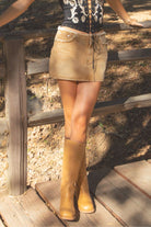 Person wearing a beige skirt and brown knee-high boots standing on wooden steps.